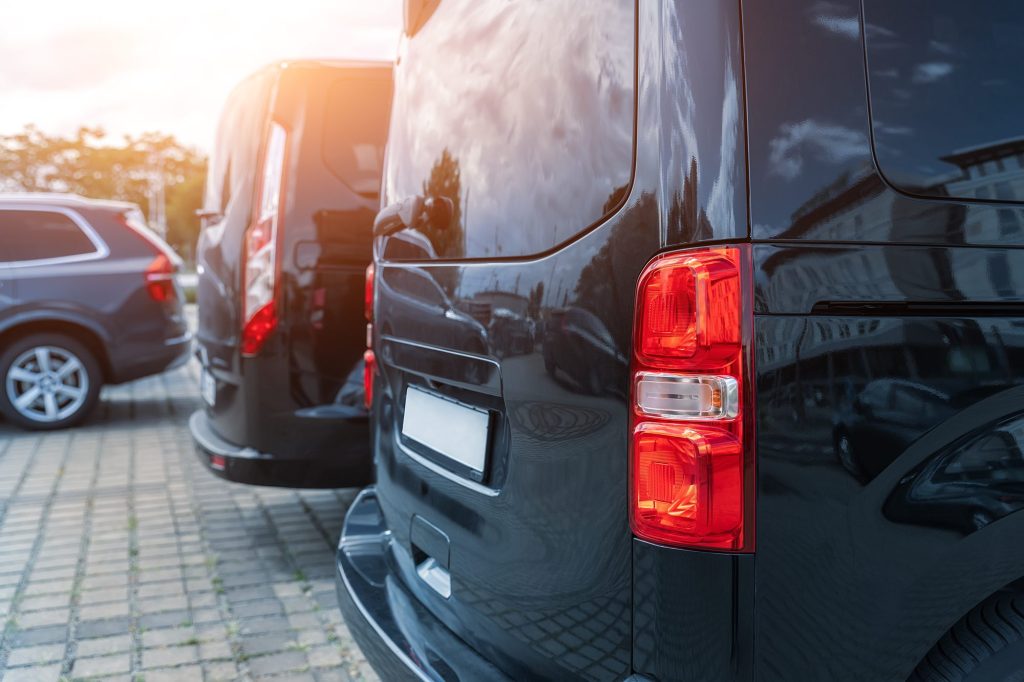 Close-up detail tail light view of many modern luxury black vans parked in row at car sale rental leasing dealer against sunset. Commericial trasfer cargo transportation company fleet. Vip charter. SSUCv3H4sIAAAAAAAACpyRy47DIAxF9yPNP0SsGykZ8mj6K9UsHHAaVAoVkI5GVf99eISK9ezwsX3ta56fH1VFZrCCkVP1DJGPhZSbdQac0Mrj5rBzg4qjKcnD0KEpAXLhtBEgSziDY6uCG3qoNikDfsUksQ7cZtGG6Tti4PDiNRJ8S6QVzymuciImfYdPEXIomN3myDJK4v/qTI/v7AYuqNhvXLgwYlAiJCPnVEquPw7NrbQGGxe6cPXQDGQooIXS3Qgm1KVo026NZ89tTG/KmbDCe3Mitb7DLMOJF6+Jma9grS/nmReDmP9kfSvmKO2igV2VcP8TIWwpbVo6DUM3ffV0PB7HvSD93iq8TlwnC/mYXQUvrYuwAcHj2EwNdDV081h3PUAN/cBqOrG+XRbecVz84V9/AAAA//8DAKIPTZWYAgAA